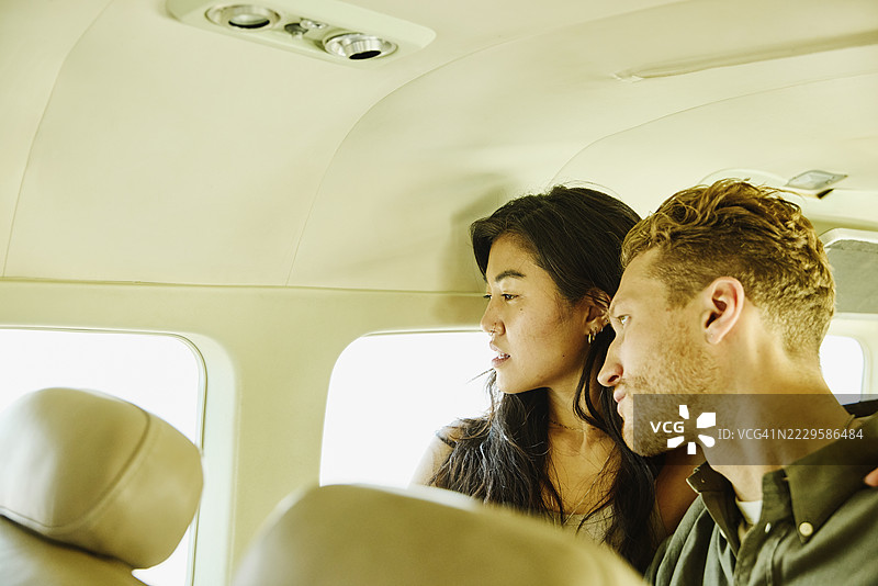 中景拍摄的情侣在飞行中透过飞机窗户眺望外面图片素材