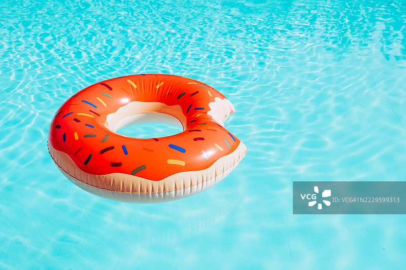 夏季游泳池背景，清澈蓝水中漂浮着充气甜甜圈，阳光明媚。极简夏季背景。图片素材