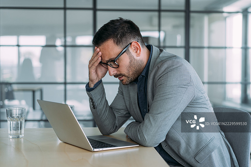 压力大的商人在办公室用笔记本电脑工作时感到头痛。图片素材