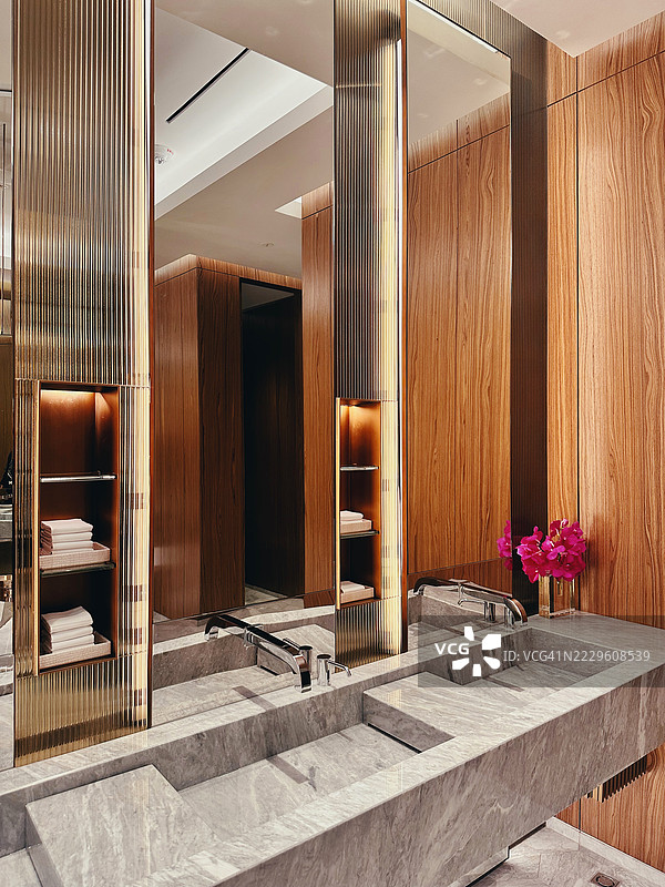奢华的公共洗手间，配有大理石洗手池、木质墙壁、金色装饰、大镜子和整齐叠放的毛巾图片素材