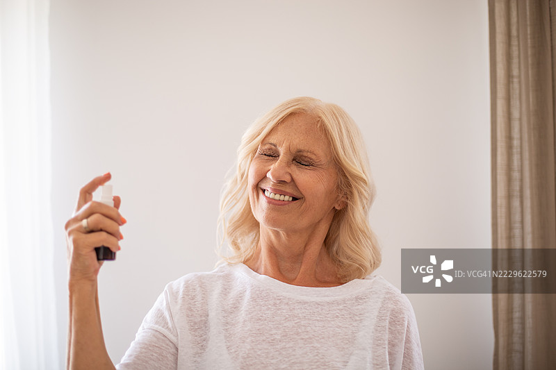 微笑的老年女性在家中喷香水图片素材