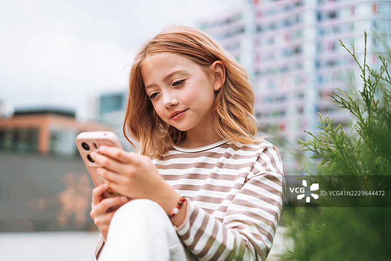 可爱的10岁女孩在街上使用智能手机，户外科技时刻图片素材