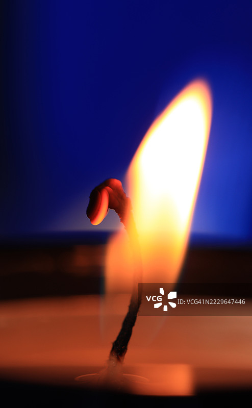 蜡烛燃烧特写，聚焦于蓝色背景上的火焰和烛芯图片素材