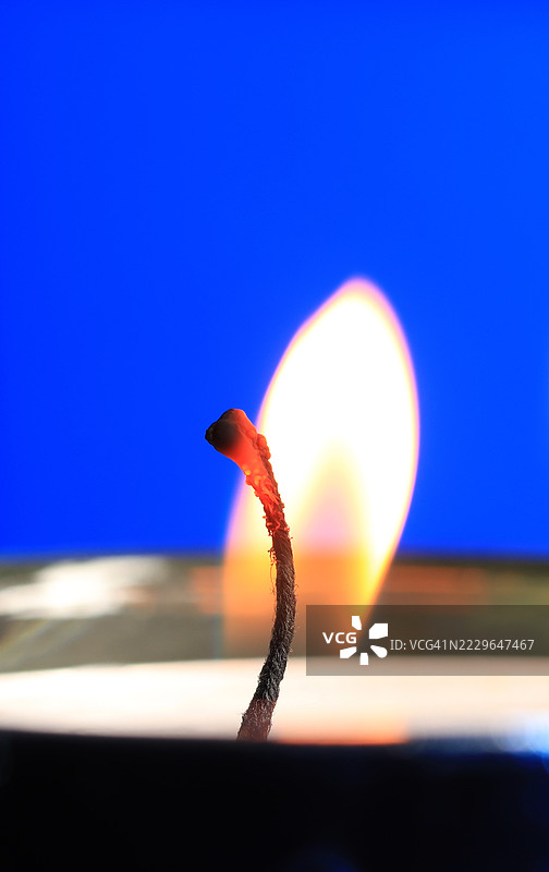 蜡烛燃烧特写，聚焦于蓝色背景上的火焰和烛芯图片素材