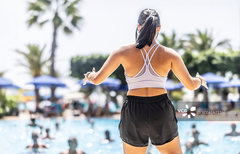 一位年轻女性运动教练正在酒店度假村的游泳池中为人们进行水中健身操。图片素材