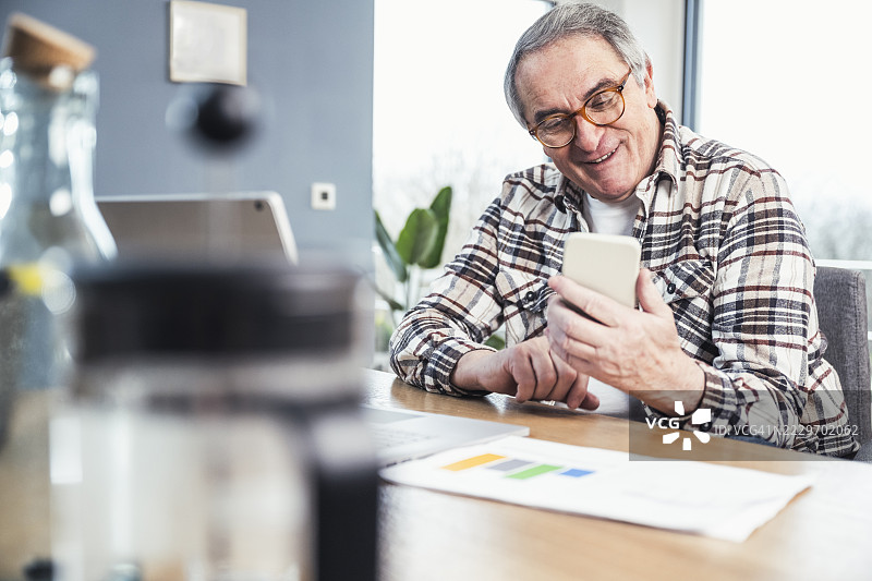 微笑的老年男子在家中通过手机发短信图片素材