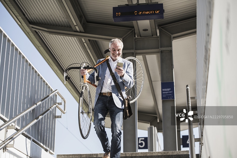 快乐的商人肩上扛着自行车，一边使用手机一边走下楼梯图片素材