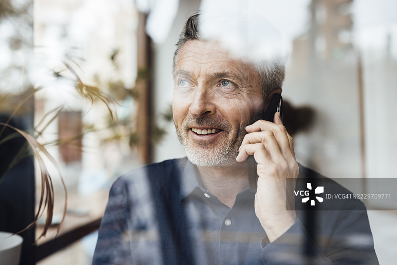 透过玻璃看到的微笑商人正在用手机通话图片素材