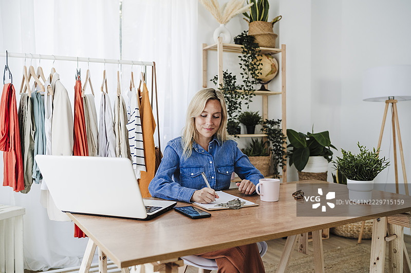 女商人在家办公桌前坐着，正在写字夹上的内容。图片素材