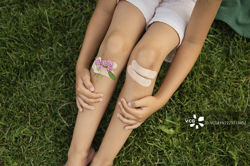 女孩在公园里坐着，膝盖上用绷带绑着花朵。图片素材