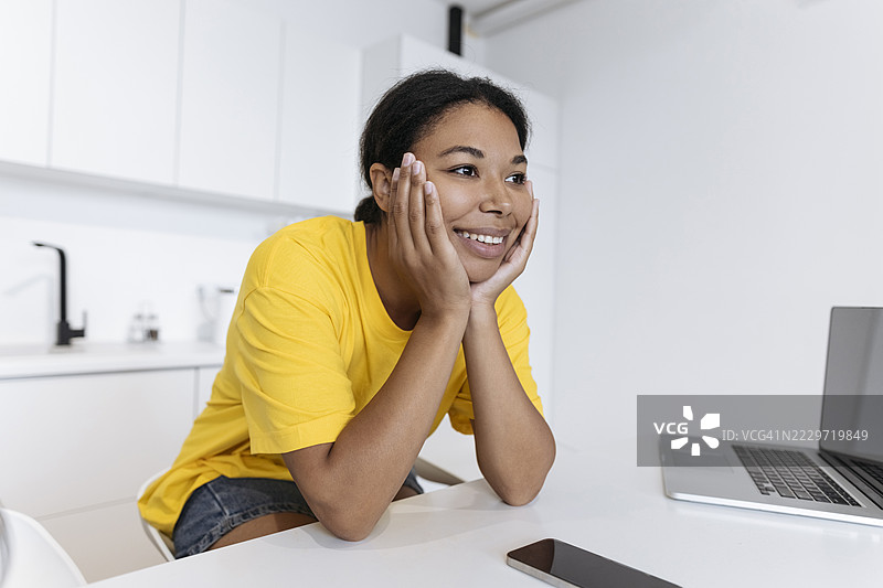 快乐的自由职业者坐在厨房的桌子旁，双手托着头。图片素材