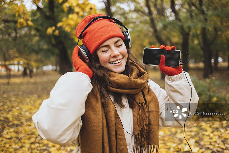 快乐的女人在公园里戴着耳机，手持手机享受音乐图片素材