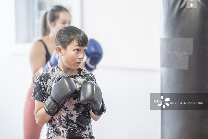 年轻男孩在明亮的工作室环境中与教练练习拳击图片素材