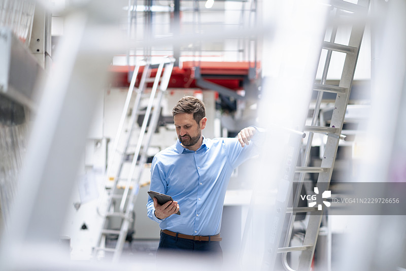商人在工业现场靠着梯子使用平板电脑图片素材