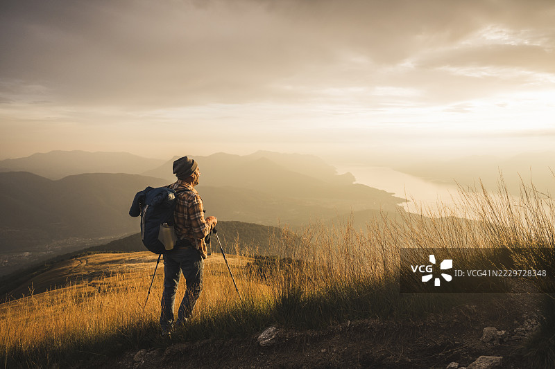 成熟男子手持登山杖和背包，凝视日出图片素材