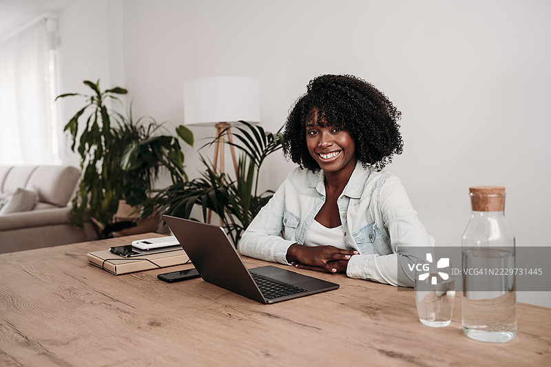 微笑的自由职业者坐在家中办公室的桌子前使用笔记本电脑图片素材