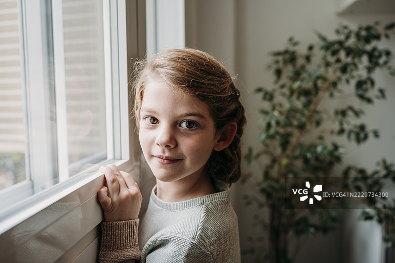 微笑的可爱女孩站在家里的窗边图片素材