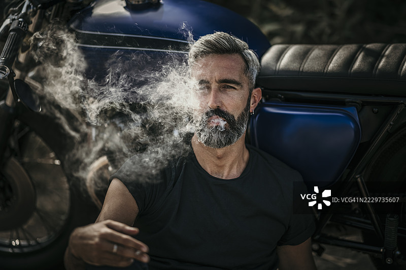 成熟男子坐在摩托车旁吸烟图片素材