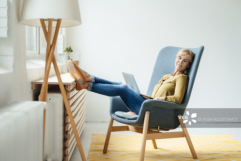 交叉着脚踝的女商人坐在扶手椅上休息图片素材