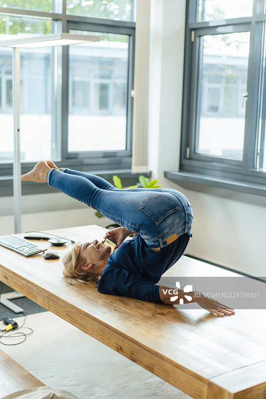 快乐的女商人在办公室做哈拉萨那瑜伽姿势并且在手机上通话图片素材