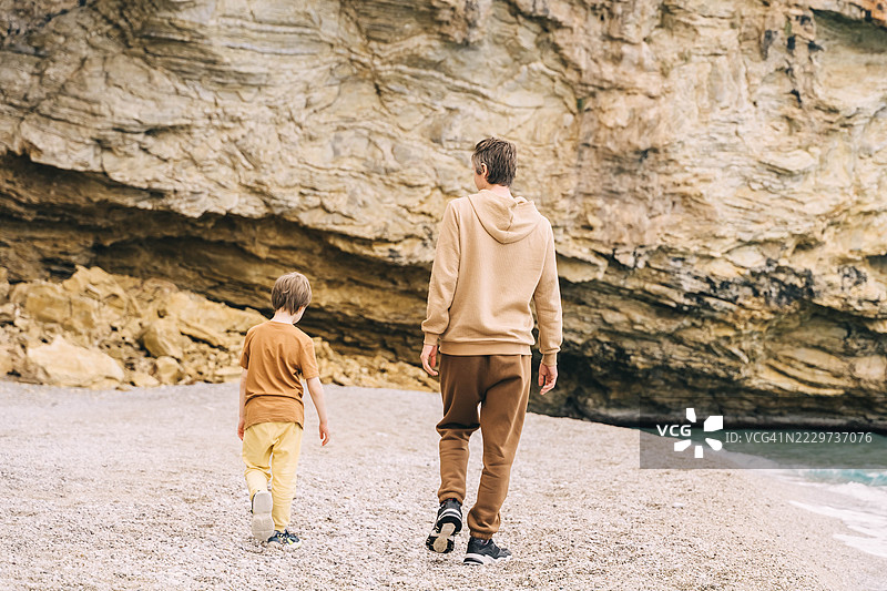 年轻父亲和小儿子在沙滩上散步，背景是美丽的岩石纹理。图片素材