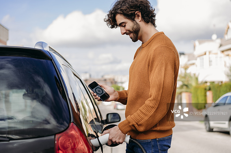 微笑的年轻男子在电动车充电站为汽车充电图片素材
