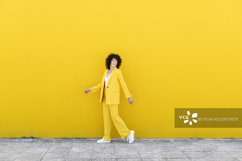 时尚女性在黄色墙壁旁的人行道上行走图片素材