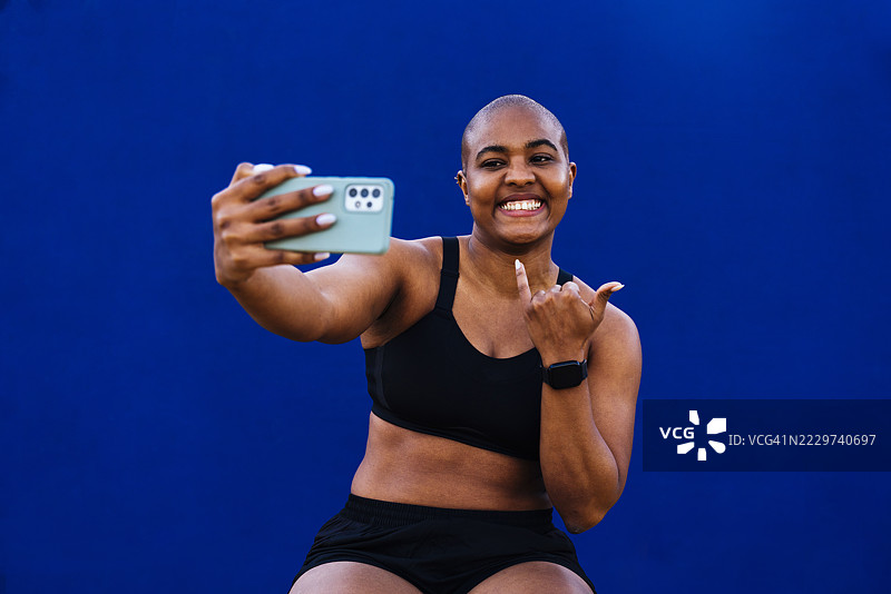 快乐的女人在蓝色墙前做手势并自拍图片素材