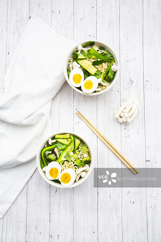 春季拉面配鸡蛋、雪豆、 zucchini 和蘑菇，摆放在白色木桌上图片素材