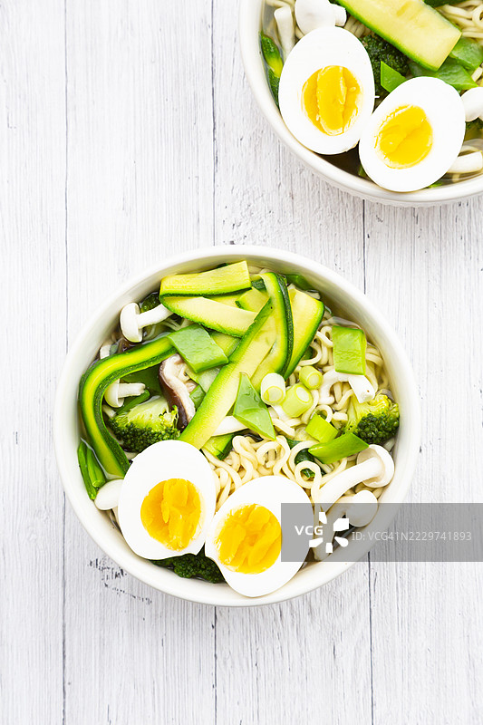 春季拉面配鸡蛋、雪豆、 zucchini 和蘑菇，盛在白色木桌上的碗里图片素材