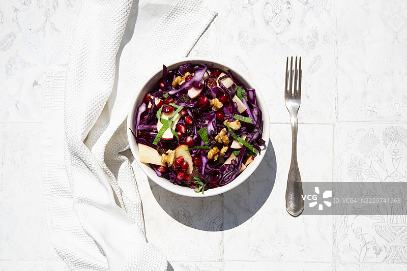 红甘蓝沙拉，配有苹果、石榴籽、薄荷、葡萄干和核桃，放在白色瓷砖上的碗里图片素材