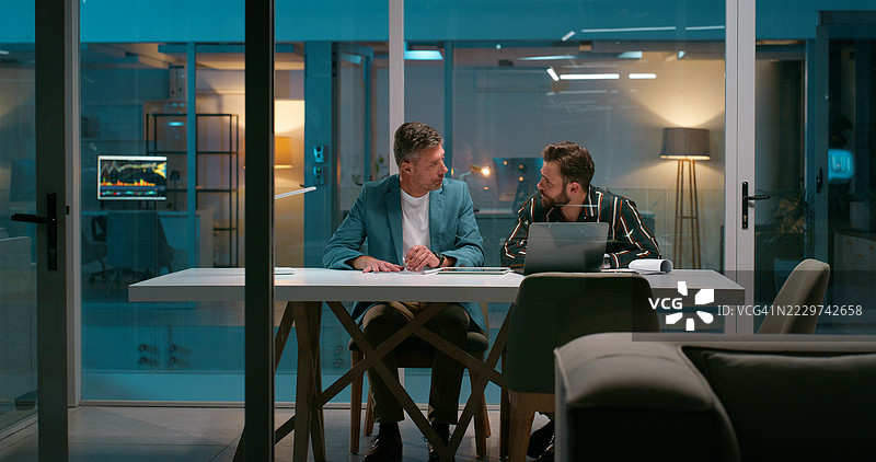 夜间办公室与商人合作，使用笔记本电脑进行项目管理。员工团队在晚上进行规划和研究，以满足行政截止日期。图片素材