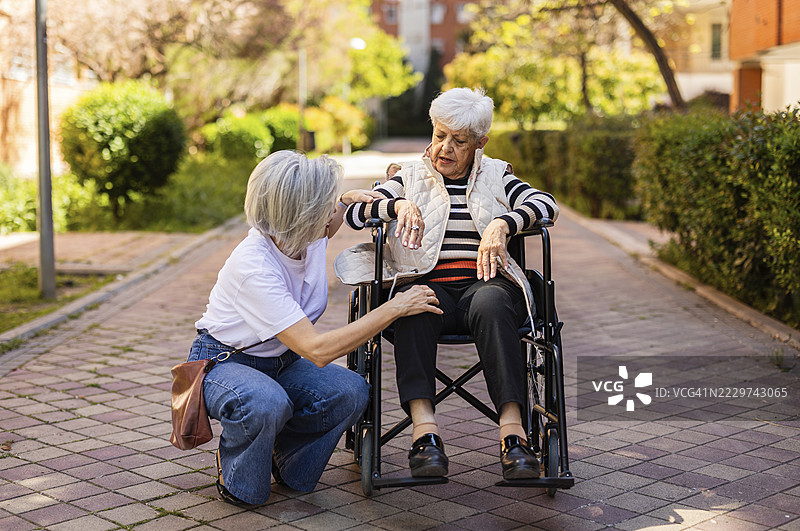 护理人员在户外与坐在轮椅上的老年女性谈话时提供支持图片素材