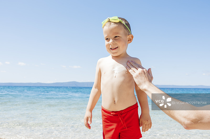 父亲在阳光明媚的海滩上给孩子涂防晒霜图片素材