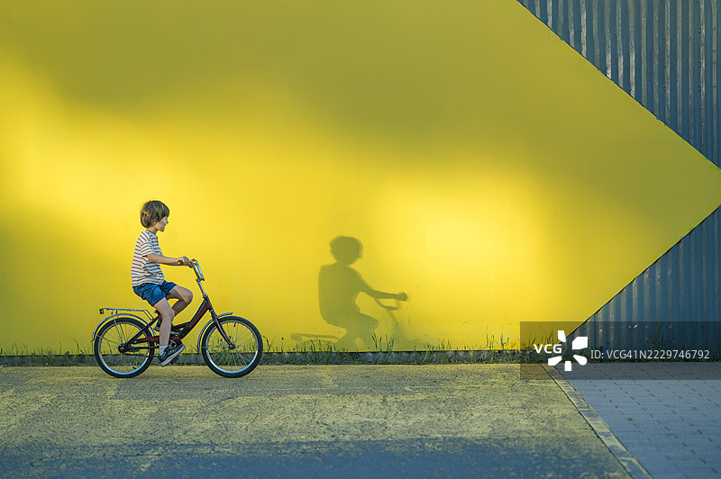 男孩在夏天骑自行车，经过黄色背景。图片素材