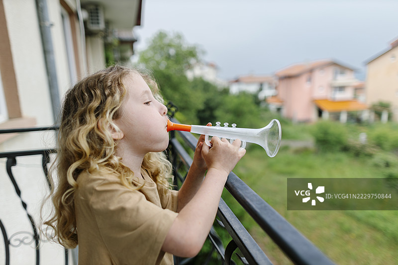 孩子在阳台上玩玩具小号，享受快乐的时光图片素材