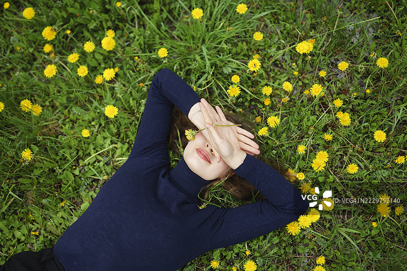 快乐的女人躺在蒲公英中，双手遮住眼睛，享受户外时光图片素材