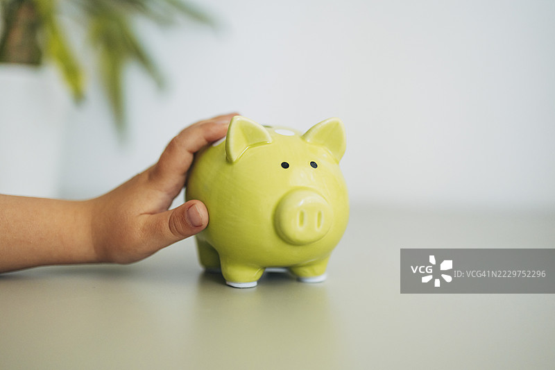 孩子的手在室内的桌子上触摸一个绿色的储蓄罐图片素材