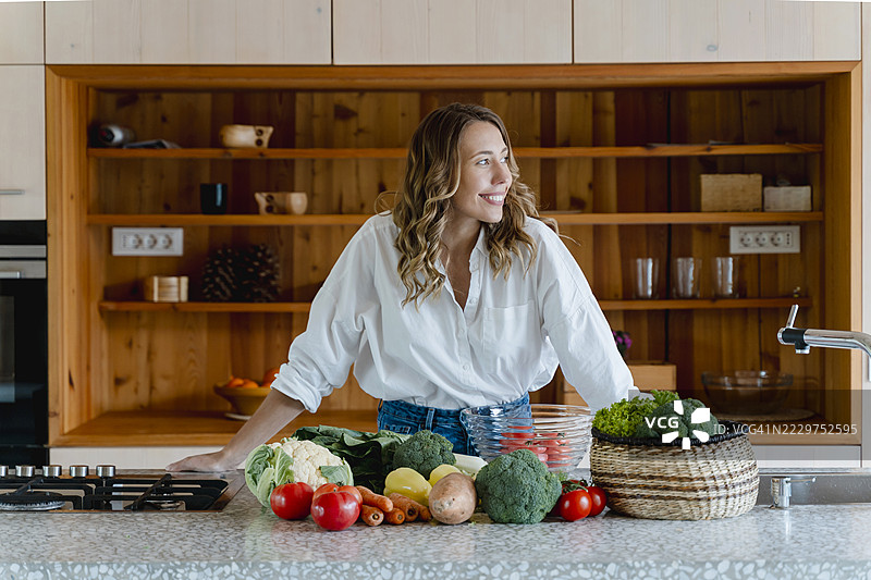 在厨房里微笑的女性与新鲜蔬菜，倡导生态生活和健康生活方式图片素材