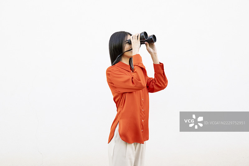 穿着橙色衬衫的女人在白色墙壁前使用望远镜图片素材