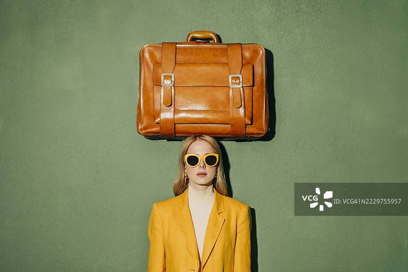 时尚女性穿着黄色夹克，手提行李箱在头顶上方图片素材
