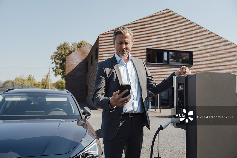 商人一边查看手机一边为电动车充电图片素材