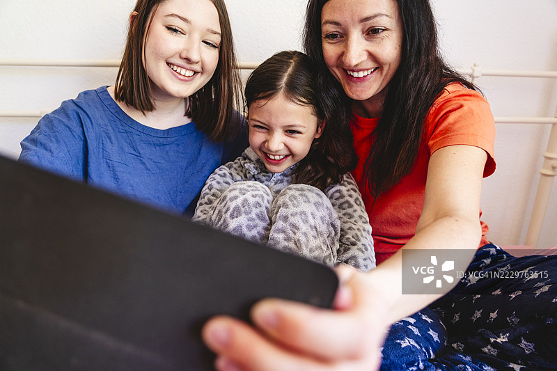 母亲和女儿们在家里床上用平板电脑自拍，增进感情。图片素材