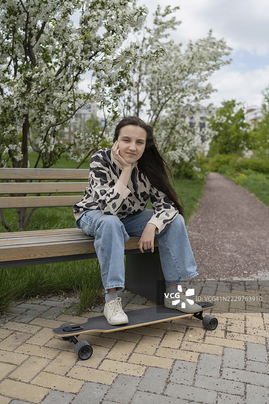 春天，青少年在公园长椅上放松，手里拿着滑板。图片素材