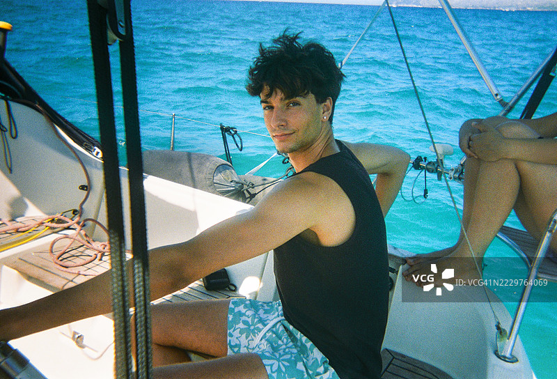 年轻男子在夏日与朋友们一起驾驶帆船。模拟胶卷效果图片素材