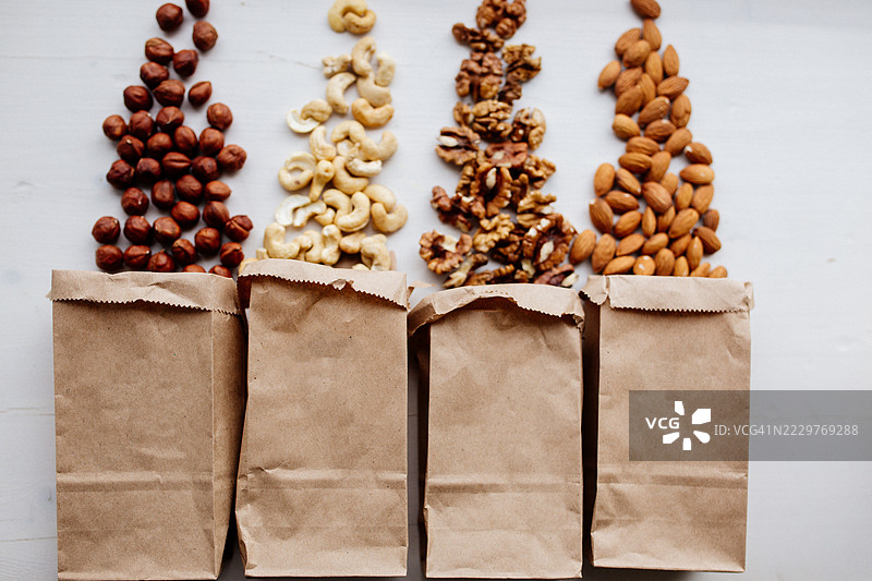 各种坚果整齐地摆放在白色背景上的牛皮纸袋旁边图片素材