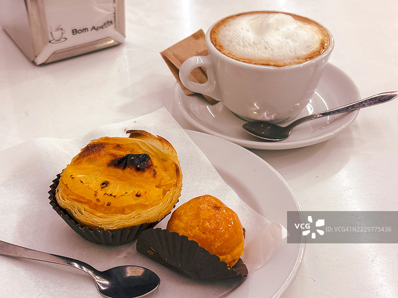桌子上放着葡萄牙糕点和一杯卡布奇诺图片素材