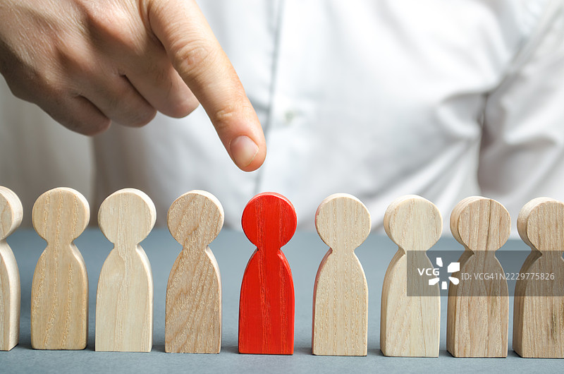 手指指向一个红色木制人物，周围是米色人物，象征着选择和领导，乌克兰图片素材
