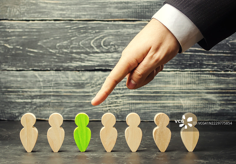 手指指向木质背景上一个绿色木制人物，周围是米色人物，乌克兰图片素材