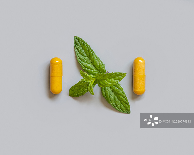 灰色背景上的黄色胶囊与新鲜薄荷叶，意大利布林迪西图片素材